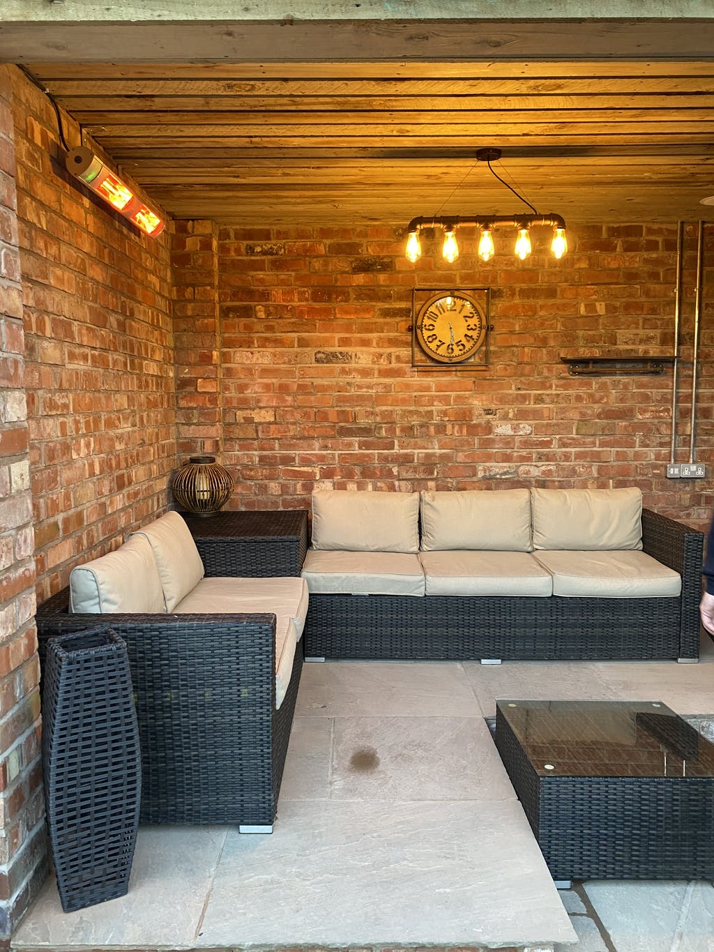 Outdoor brick patio lounge area with black wicker furniture, retro lighting and the KMH-30R 3KW Infrared Wall Mounted Outdoor Garden Heater mounted on the wall