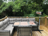 Load image into Gallery viewer, Lifestyle photograph of a wooden patio deck with a corner grey wicker sofa and glass top wicker table with the KMH-3000R 3KW Free Standing Infrared Heater and greenery in the background