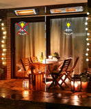 Load image into Gallery viewer, Outdoor stone patio area at night lit with fairy lights surrounding a wooden table with a set of four chairs. A side by side image is seen comparing the -80% low glare of the KMH-30R 3KW Infrared Wall Mounted Outdoor Garden Heater to a competitor brand.