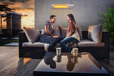Load image into Gallery viewer, A couple sitting and chatting on their wicker sofa in a roof outdoor lounge area with the Silver KMH-20R 2KW Wall Mounted Infrared Outdoor Heater mounted in the background