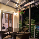 Load image into Gallery viewer, Outdoor balcony and patio area at night with four wicker chairs surrounding a black glass circular table, potted hanging plants and the Silver KMH-20R 2KW Wall Mounted Infrared Outdoor Heater mounted on a beam